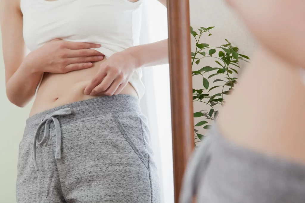 鏡の前でお腹まわりをつまみ体型をチェックする女性。ダイエットを意識した自己確認の様子。