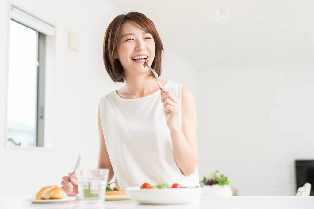 明るい部屋で食事を楽しみながら笑顔を見せる女性。前向きに食事と向き合う様子。