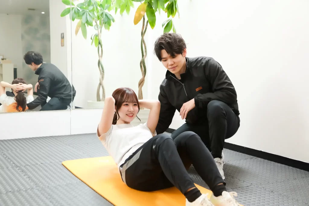 パーソナルトレーナーのサポートを受けながら腹筋トレーニングを行う女性。